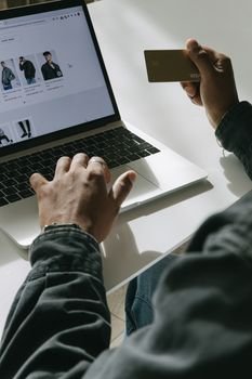 Person shopping online with credit card on a laptop in a bright setting.